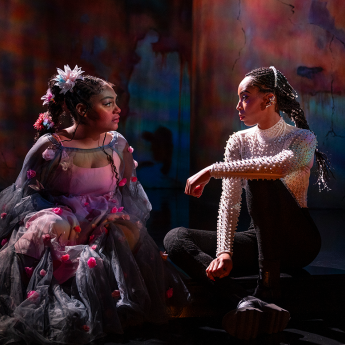 Ariana Burks and Aeriel Williams sit on the Court stage in costume will looking intently at each other.